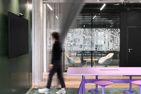 Modern office interior with a person walking past a purple table and a wall-mounted screen