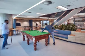 Modern office space featuring a billiards table, seating areas, and people engaging in activities