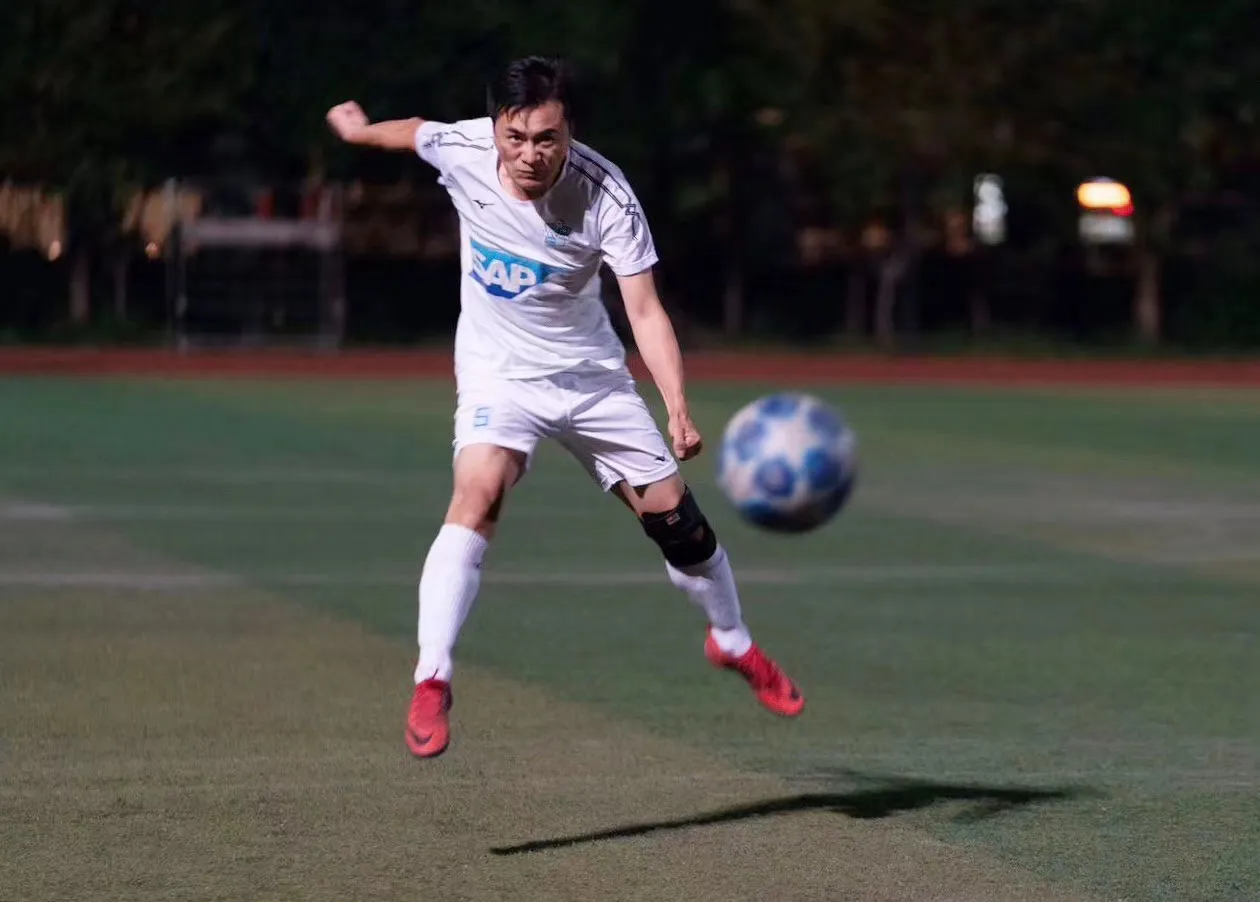 An SAP employee kicking a football during a match on an outdoor field.