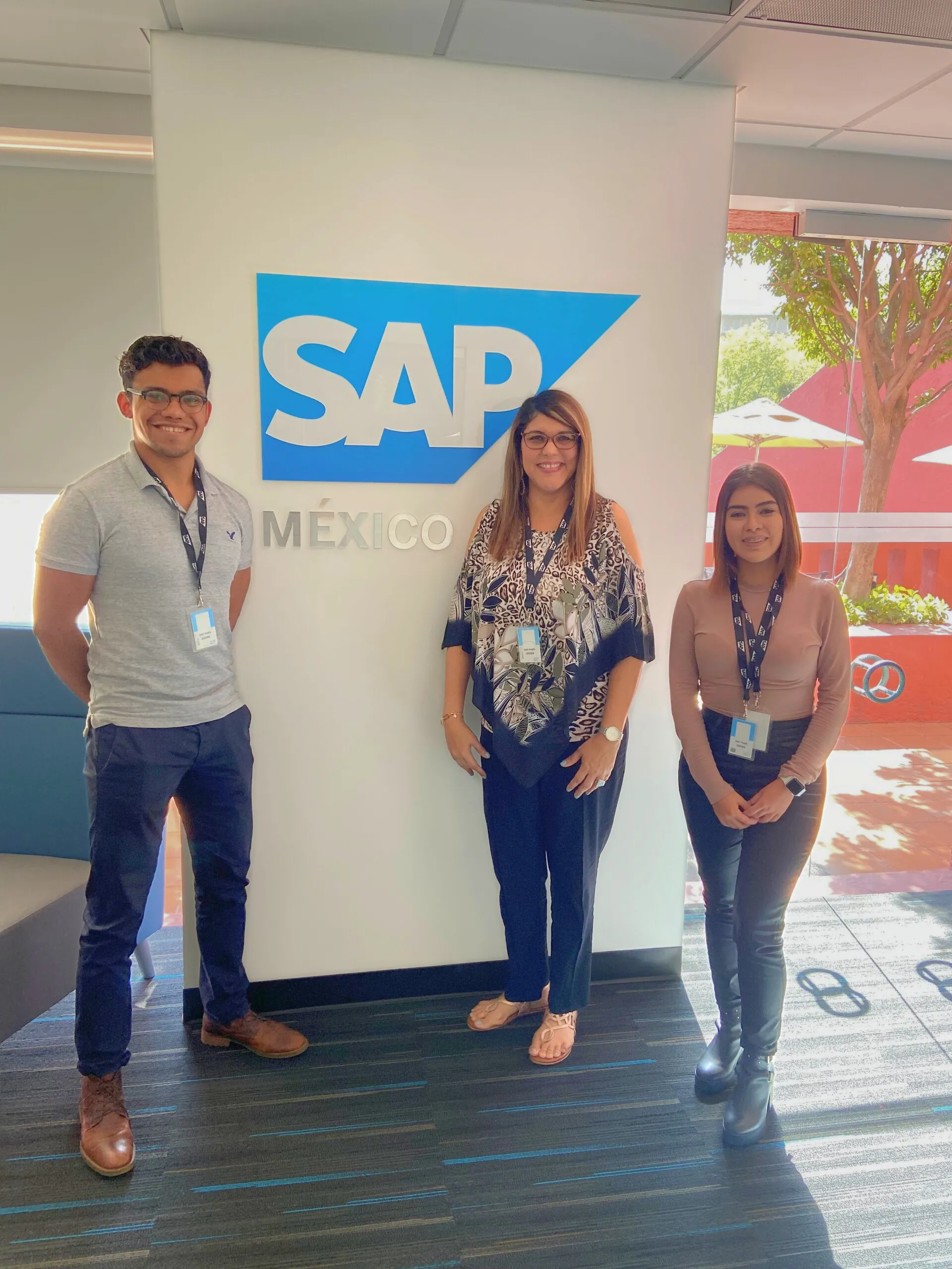 Cristina, center, stands with two team members in front of an SAP México sign.