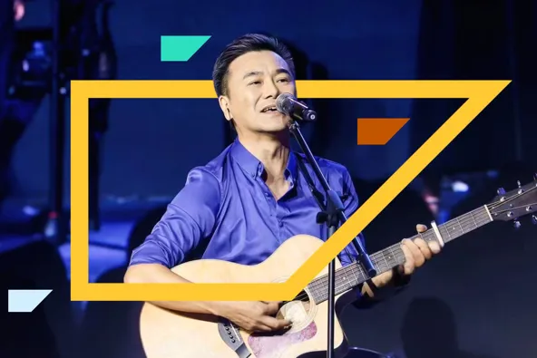 A man in a blue shirt singing and playing guitar on stage