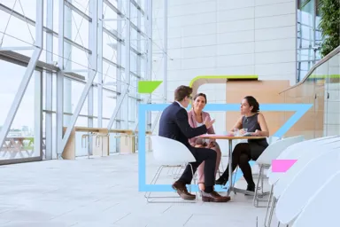 Three professionals engaged in a discussion at a modern table in a bright, open space