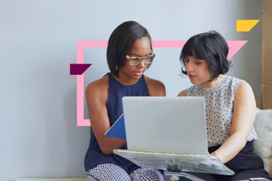 Two women collaborating on a laptop in a modern office setting