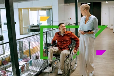 A man in a wheelchair converses with a woman in a modern office setting